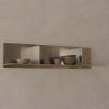 Three ceramic bowls on a metallic shelf against a beige wall