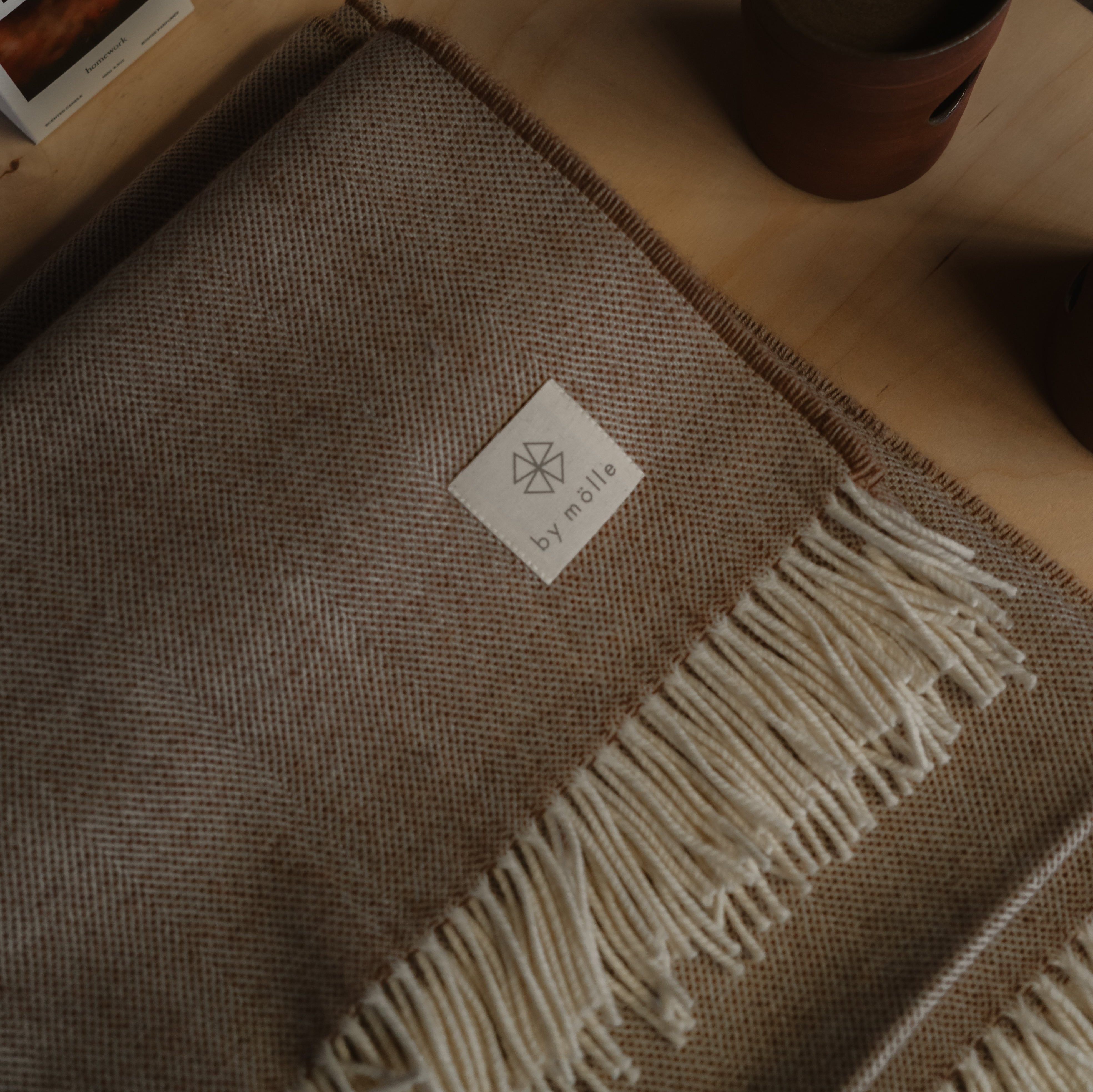 Lambswool Plaid in Cocoa van By Mölle – 100% Merino lamswol geweven in een klassiek visgraatpatroon, met een combinatie van natuurlijk crèmekleurige en warme bruine tinten. Met een afmeting van 140 x 200 cm is dit lichte maar warme plaid vervaardigd in Europa en machinewasbaar op een wolprogramma. Perfect om een gezellige sfeer aan je woonkamer toe te voegen.