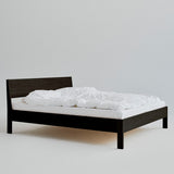 Ejer Bed Frame van RYE beschikbaar in geolied eiken, zwart gebeitst eiken of gerookt eiken, met een minimalistisch ontwerp, strakke lijnen en een licht hellend hoofdeinde, ontworpen voor een rustige en rustgevende slaapomgeving.