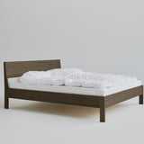 Ejer Bed Frame by RYE available in oiled oak, black stained oak, or smoked oak finishes, featuring a minimalist design with clean lines and a slightly inclined headboard, crafted for a tranquil and restful sleep environment