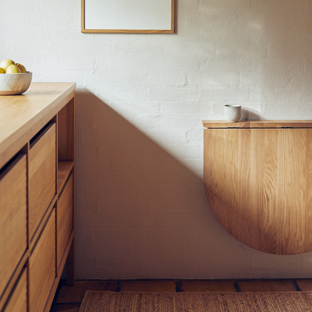 Minimalistische inklapbare wandtafel van massief eikenhout met slank frame en onzichtbaar scharniermechanisme. Ovaal tafelblad dat je eenvoudig inklapt, perfect voor compacte ruimtes.