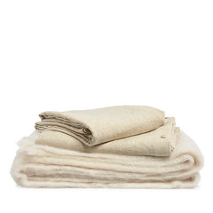 By Mölle's wheat linen duvet cover, crafted from 100% pre-washed European flax linen, features a natural chambray weave blending warm beige and off-white tones. The breathable and hypoallergenic fabric offers year-round comfort and is available with either wooden buttons or a tuck-in flap closure