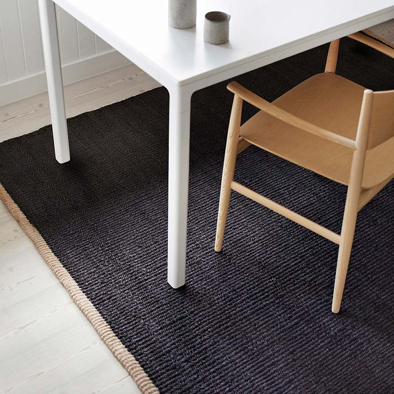 Nest vloerkleed van Armadillo, handgeweven van 100% natuurlijke jute met zorgvuldig afgewerkte uiteinden, verkrijgbaar in de kleuren Natural en Charcoal, biedt een minimalistisch ontwerp dat warmte en textuur toevoegt aan woonruimtes.