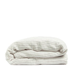 By Mölle's Cocoa Stripe linen duvet cover, crafted from 100% pre-washed European flax linen, features a warm white base with subtle cocoa-colored stripes. The chambray weave adds depth and character, offering a breathable and hypoallergenic fabric suitable for year-round comfort. Available with either wooden buttons or a full-width tuck-in flap closure.