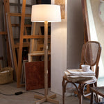 Wooden floor lamp in a room with chairs and a table.