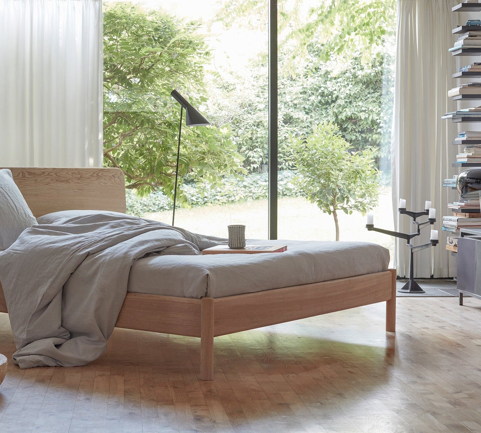 Alken bedframe van massief eikenhout in een kamer met uitkijk op een grote groene tuin.