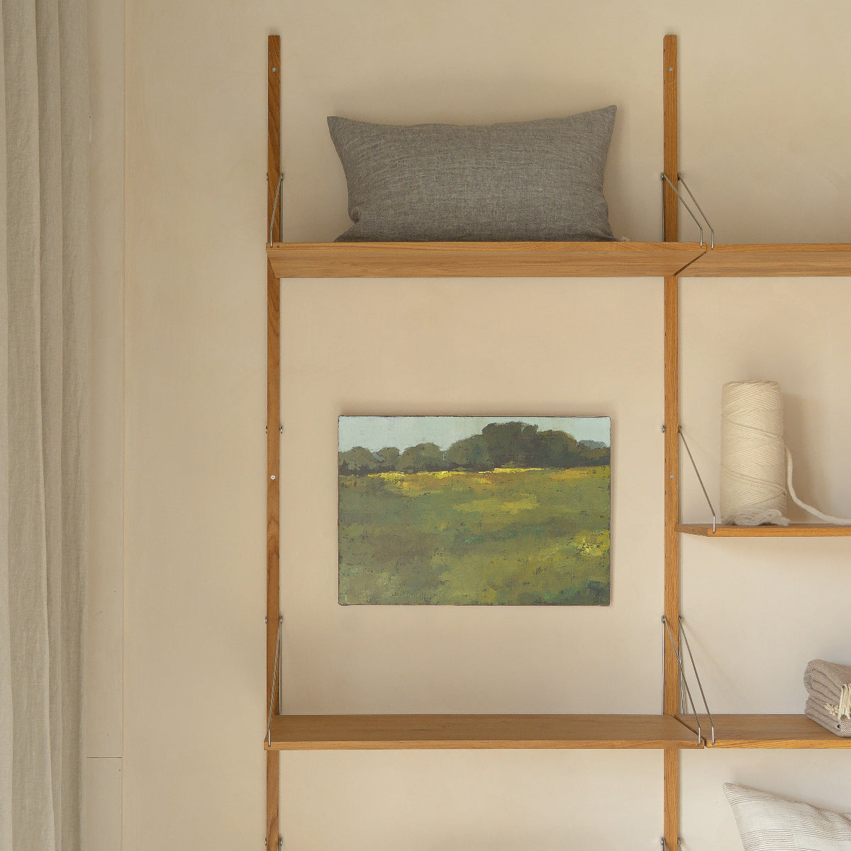 Wooden shelf against a wall with decorative items including a painting and pillows.