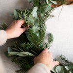 Person arranging greenery in a wreath on a neutral background
