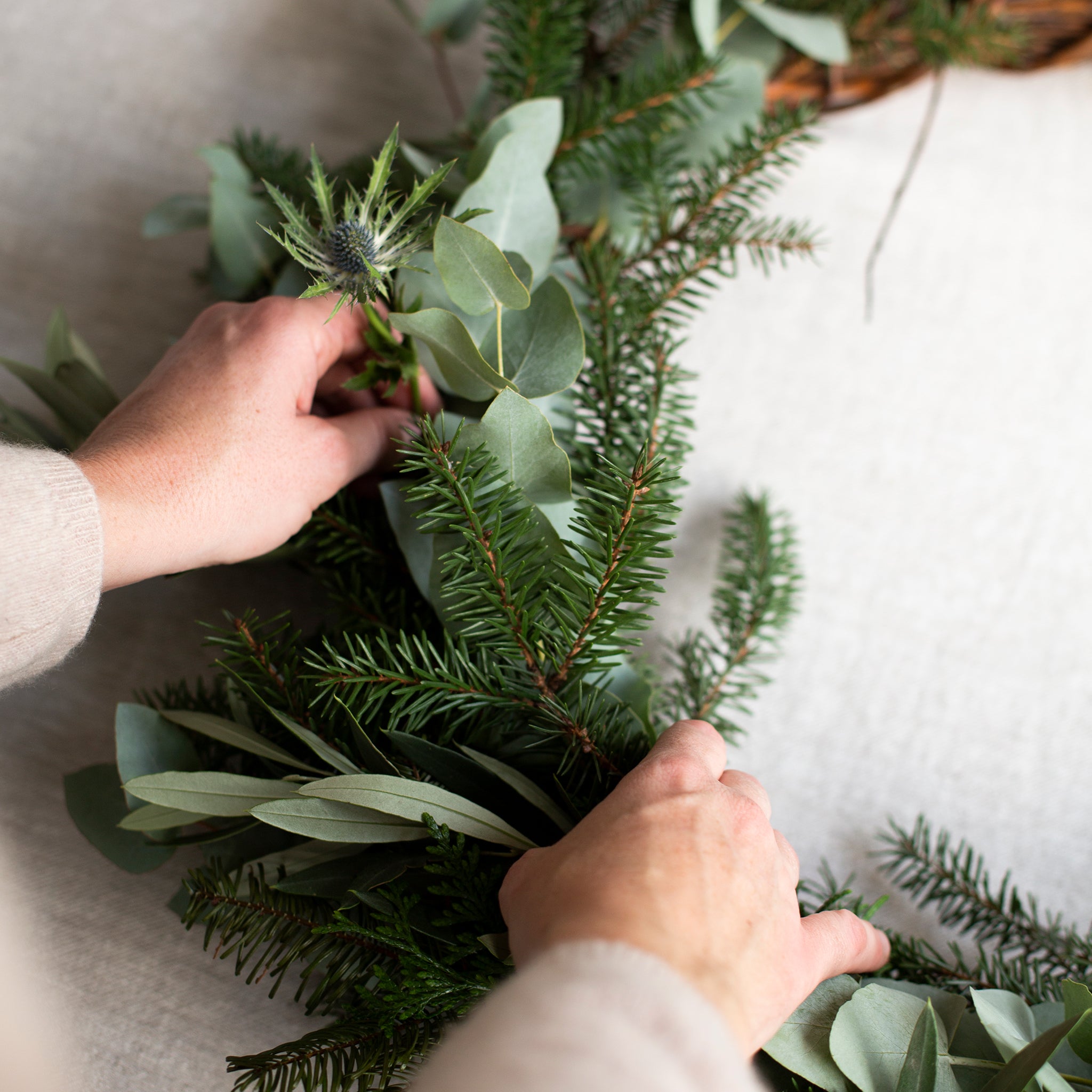 Person arranging greenery in a wreath on a neutral background