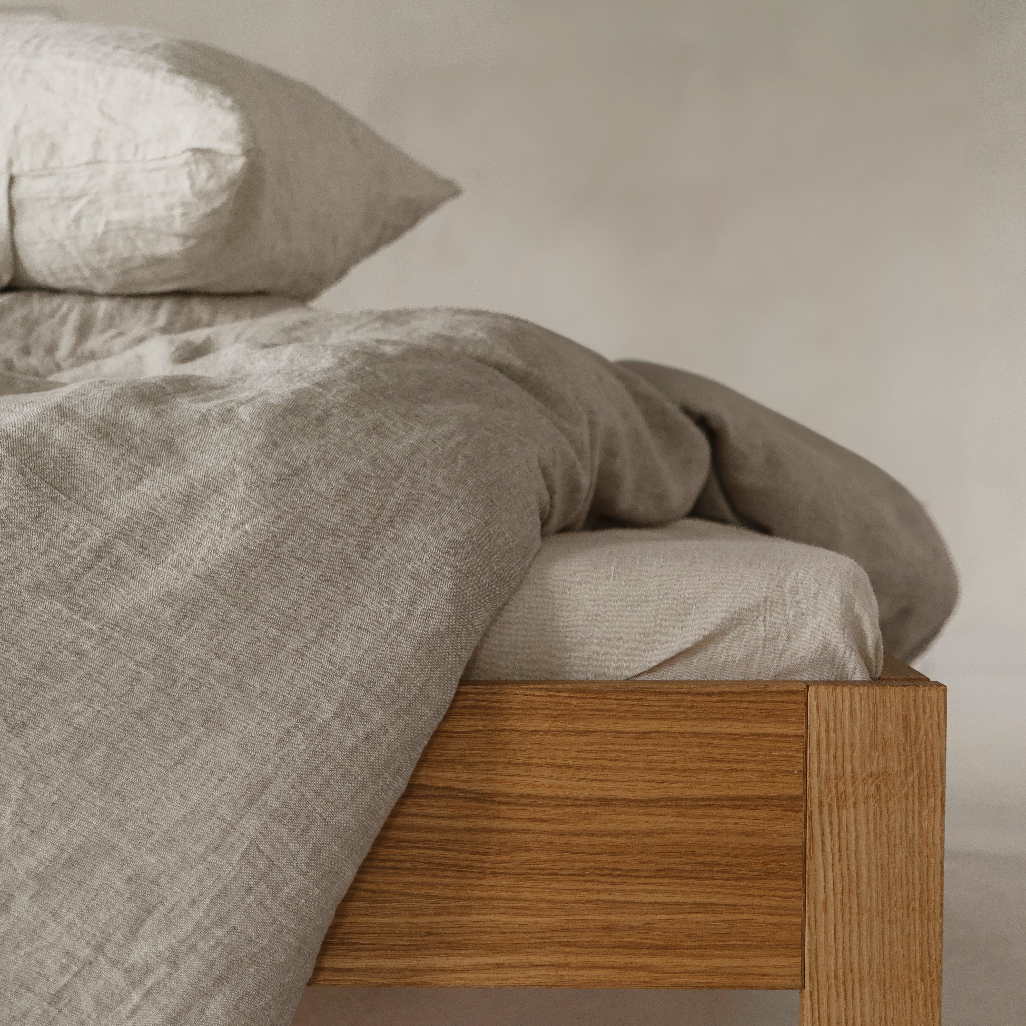 Bed with wooden frame and beige bedding against a neutral wall