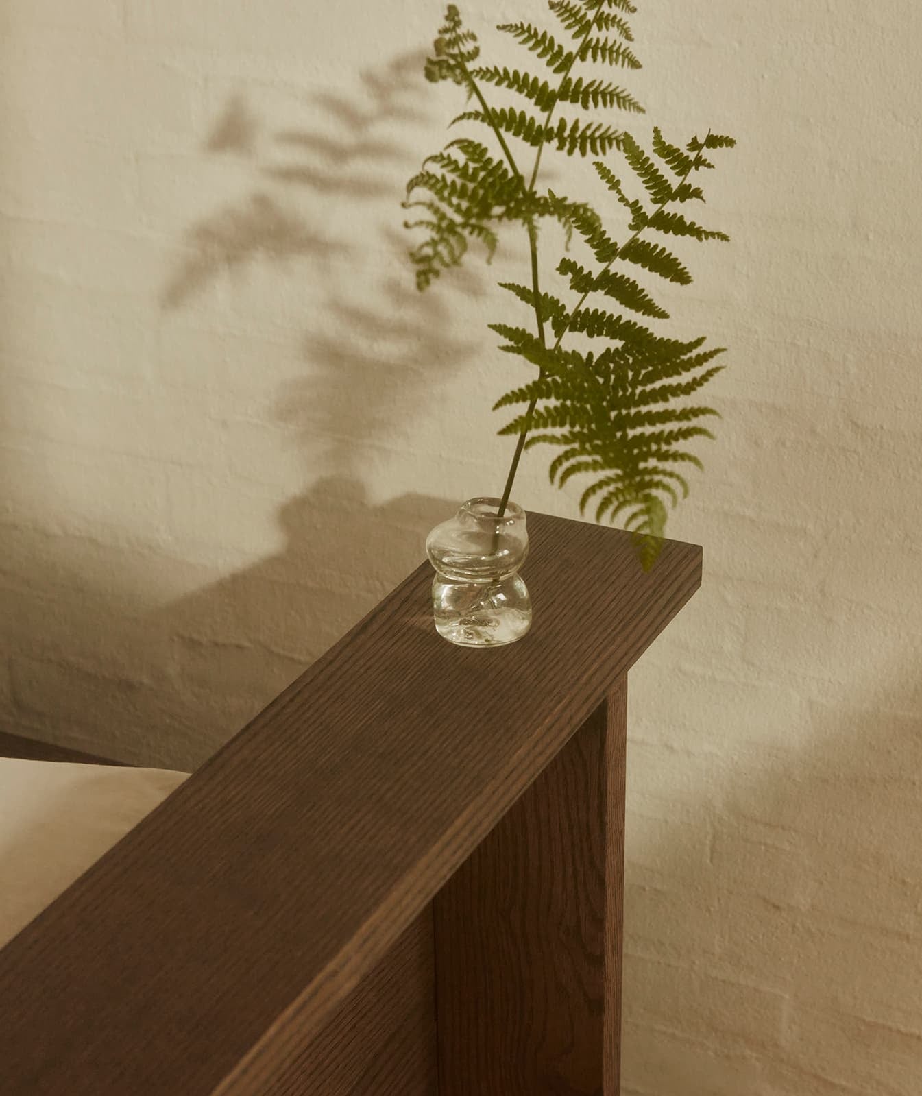 Glaasje met een varen op de houten bedrand van het Hem bedframe. Scandinavisch design, handgemaakt in Denemarken.