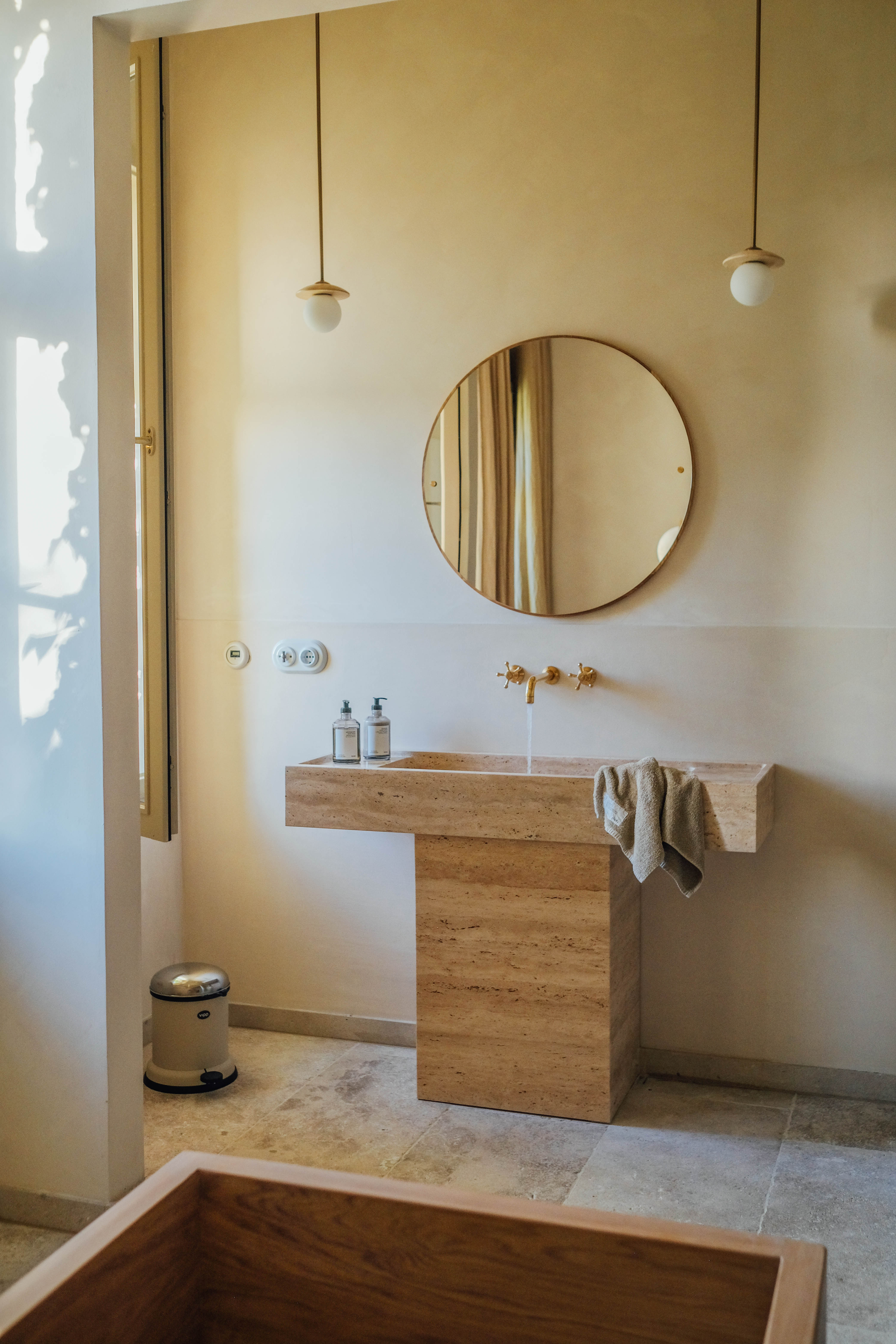 Beige badkamer met ronde spiegel en houten badkuip.