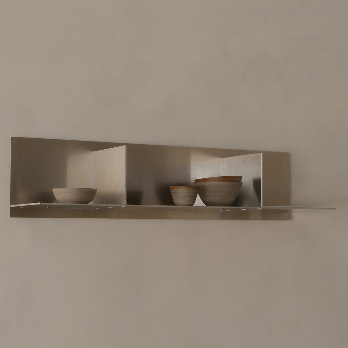 Three ceramic bowls on a metallic shelf against a beige wall