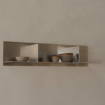 Three ceramic bowls on a metallic shelf against a beige wall