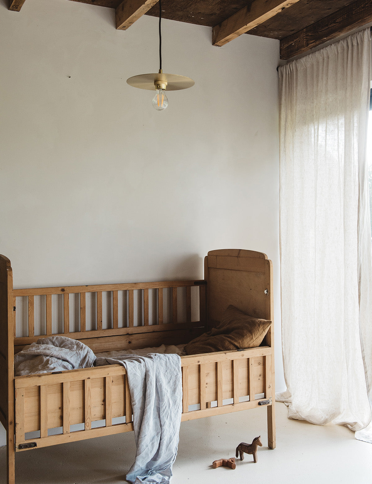 Linnen gordijnpaneel op een kinderkamer met een houten ledikantje.