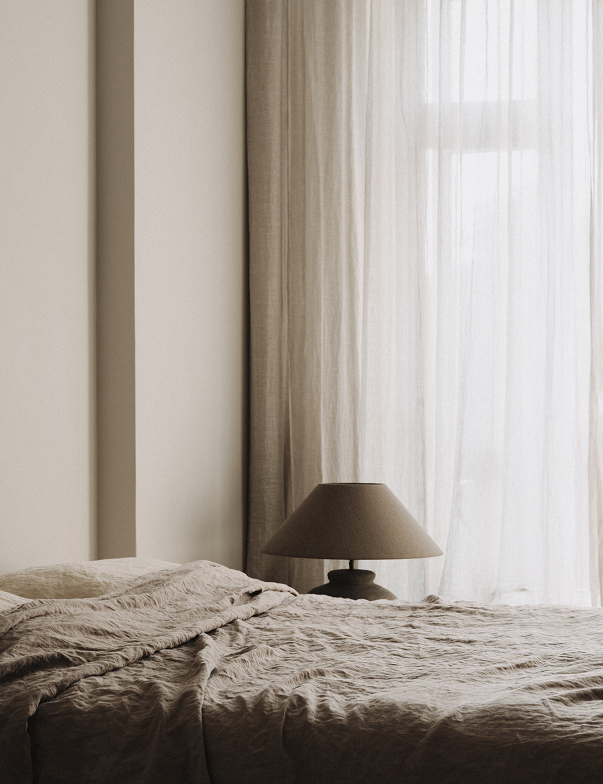 Slaapkamer met sheer linnen gordijn en puur linnen beddengoed van By Mölle in de kleur flax en sea shell.