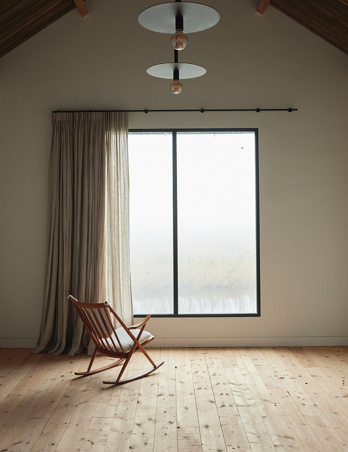 By Mölle linnen gordijn flax in een modern interieur met houten vloer en groot raam met uitzicht op het water.