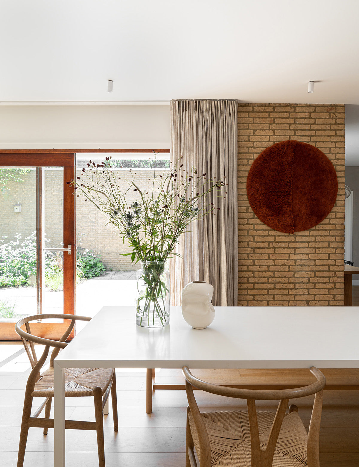 Leefruimte met witte tafel, wishbone stoelen en flax linnen gordijnen van By Mölle.