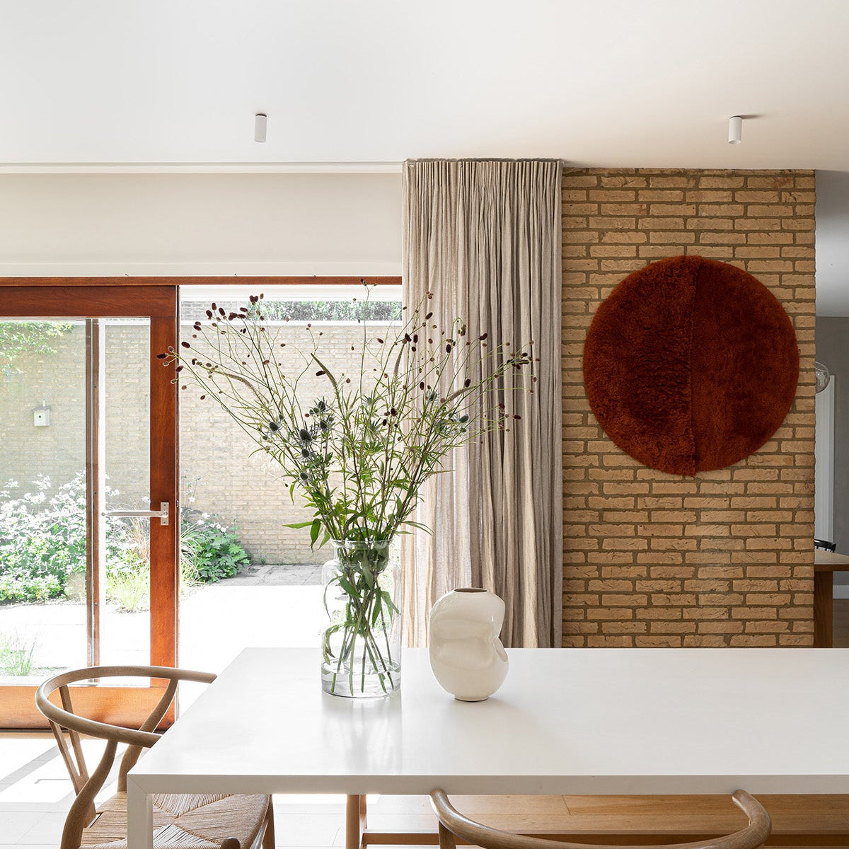 Leefruimte met witte tafel, wishbone stoelen en flax linnen gordijnen van By Mölle.
