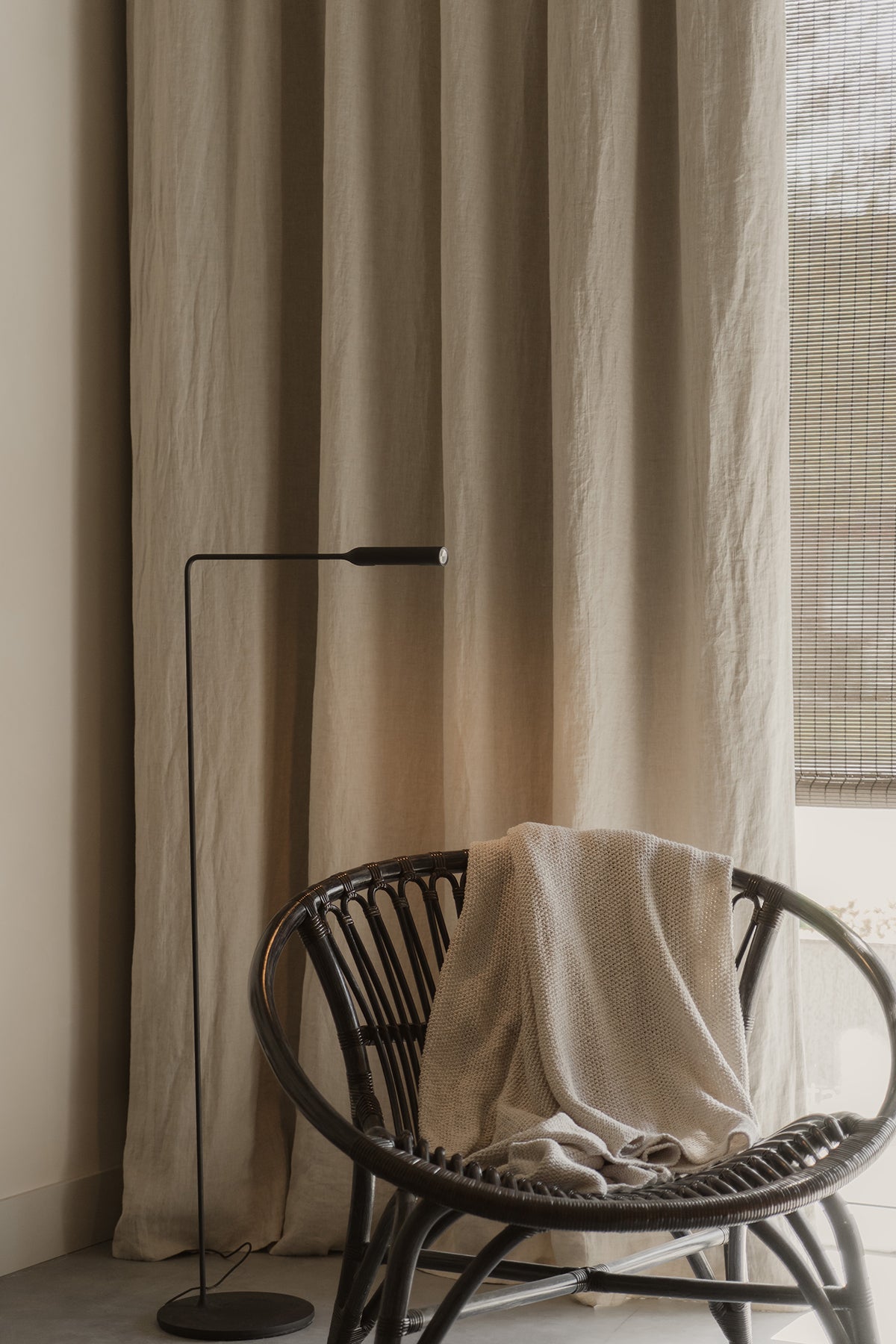 Rotan stoel met gerecycled denim plaid, een zwart staand leeslampje en puur linnen gordijnen in de beige tint sea shell van By Mölle.