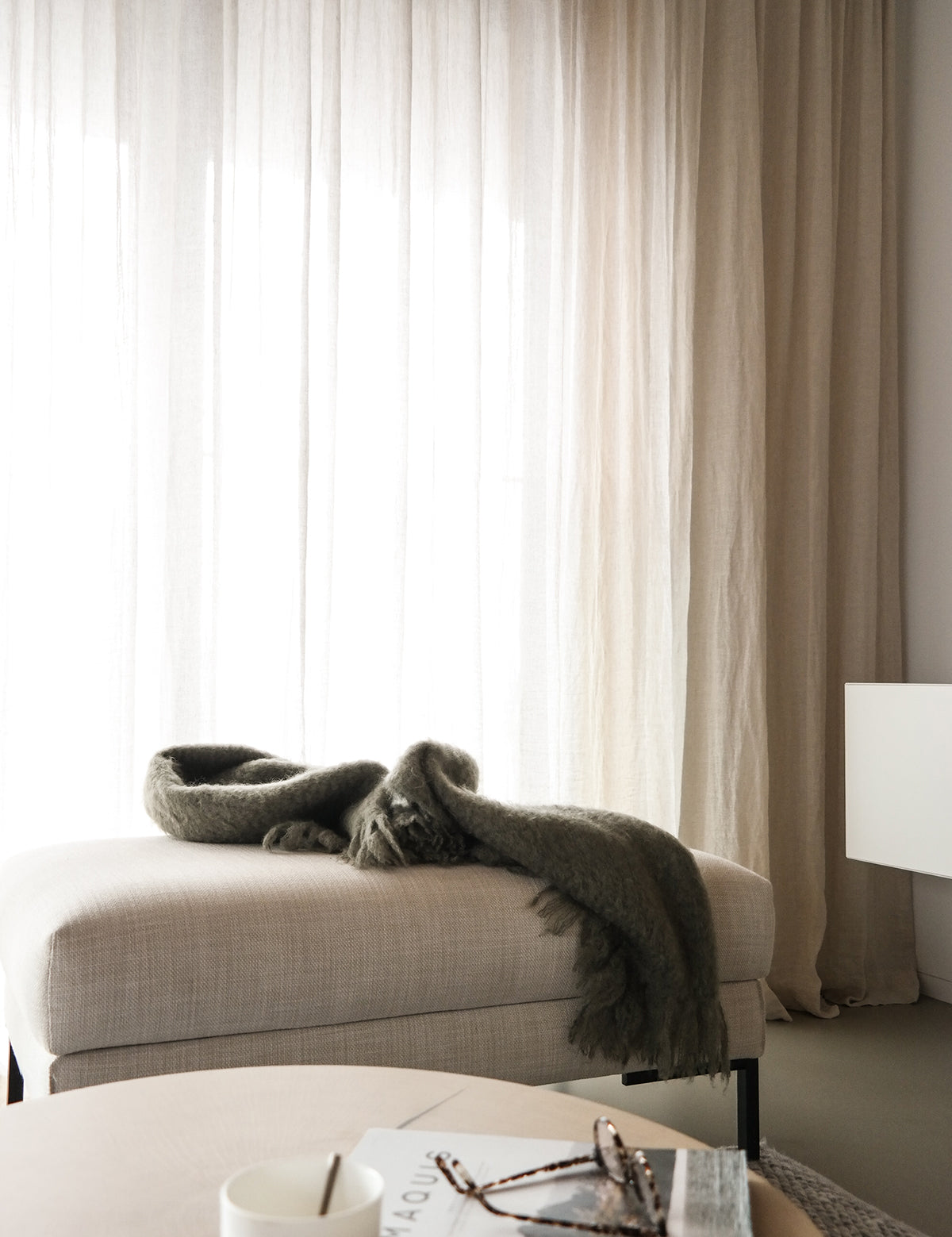 Woonkamer met By Mölle sheer linnen gordijnen in flax, een beige kruk en houten tafel.