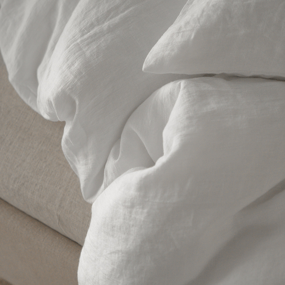 Close-up of By Mölle pure white linen bedding on a beige bed frame