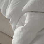 Close-up of By Mölle pure white linen bedding on a beige bed frame