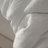 Close-up of By Mölle pure white linen bedding on a beige bed frame