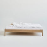 Minimalistisch houten bed Alken zonder hoofdbord, met wit beddengoed op een effen achtergrond.