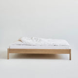 Minimalistisch houten bed Alken zonder hoofdbord, met wit beddengoed op een effen achtergrond.