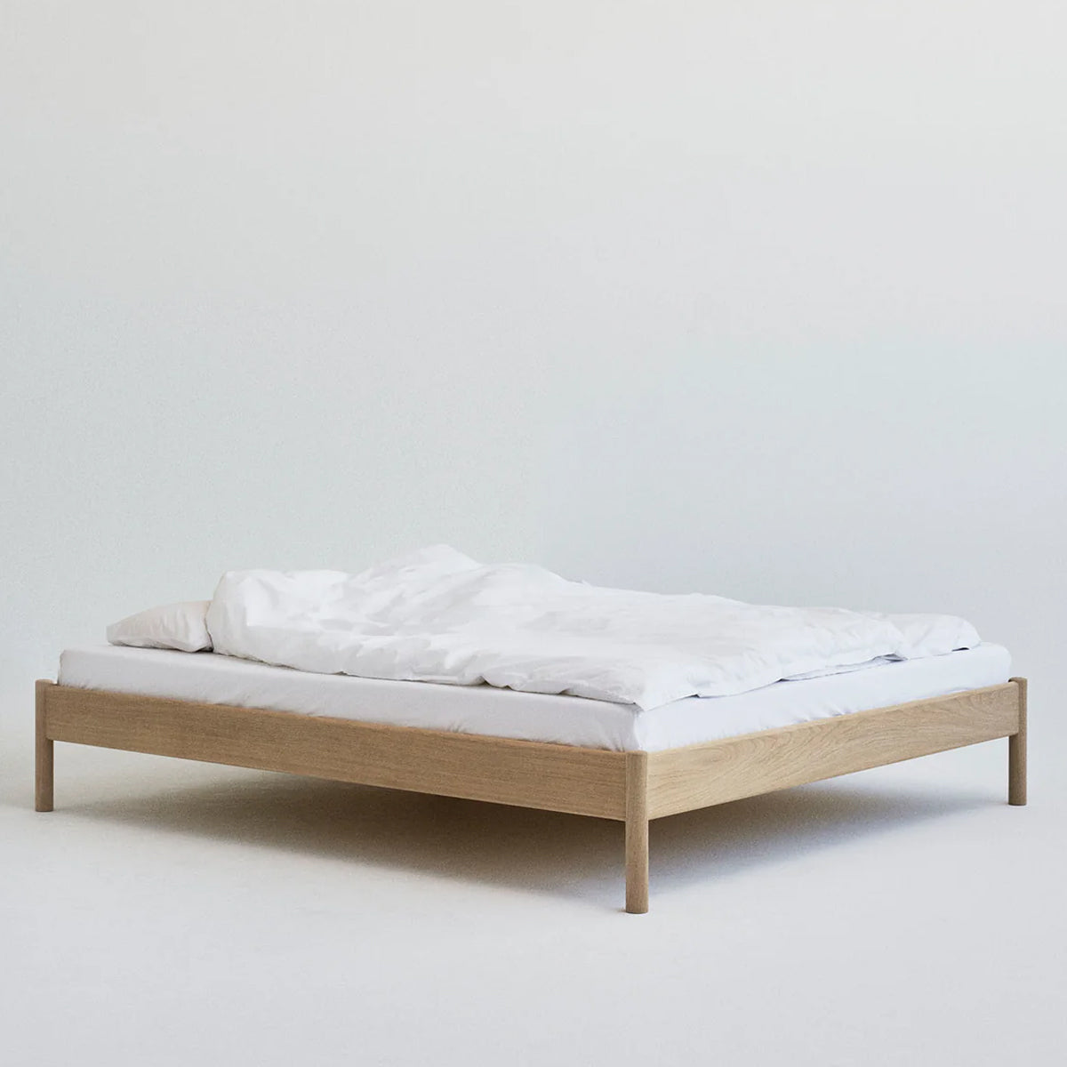 Massief houten bed met wit beddengoed op een effen achtergrond.