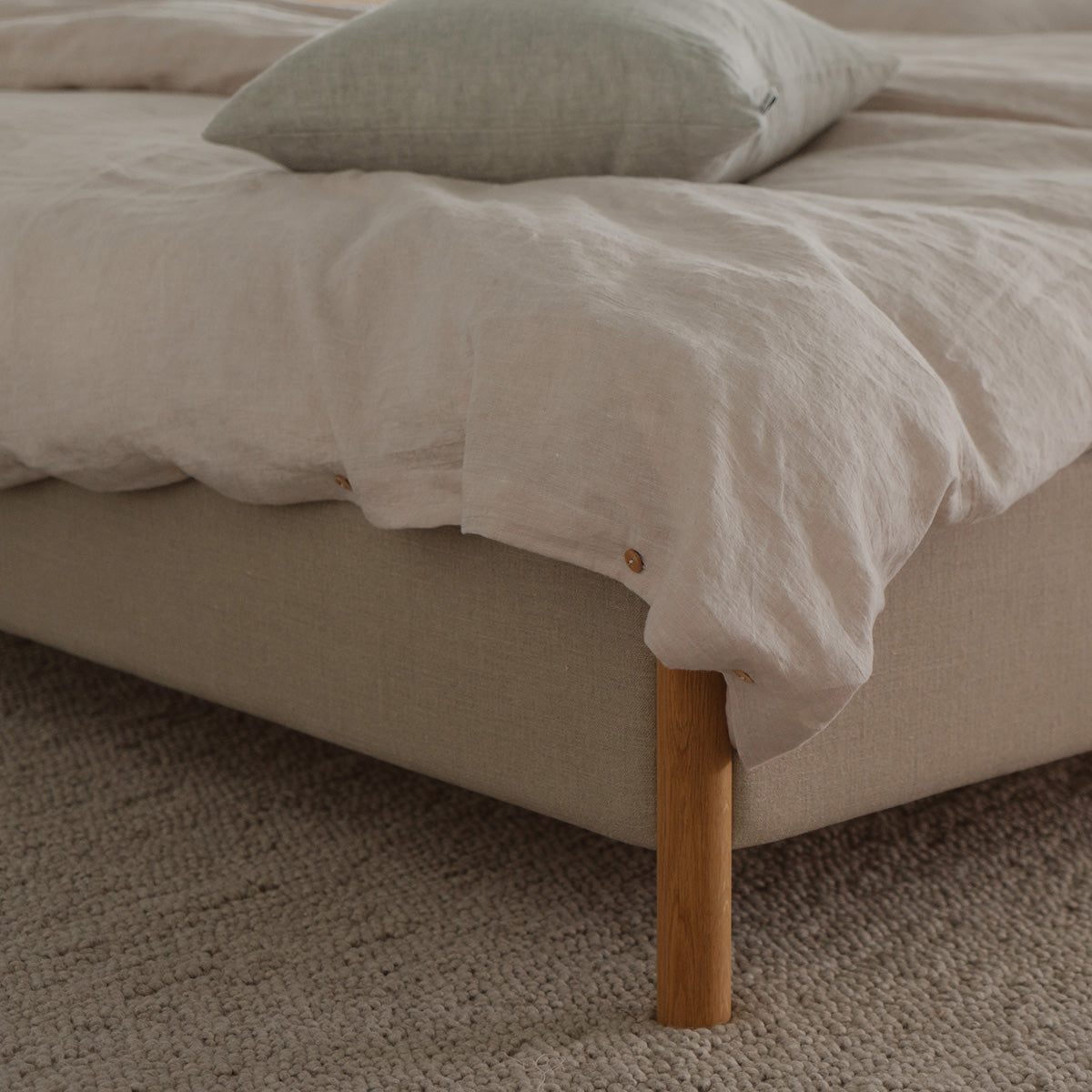 Veng bed frame met massief houten poten en beige linnen bekleding.