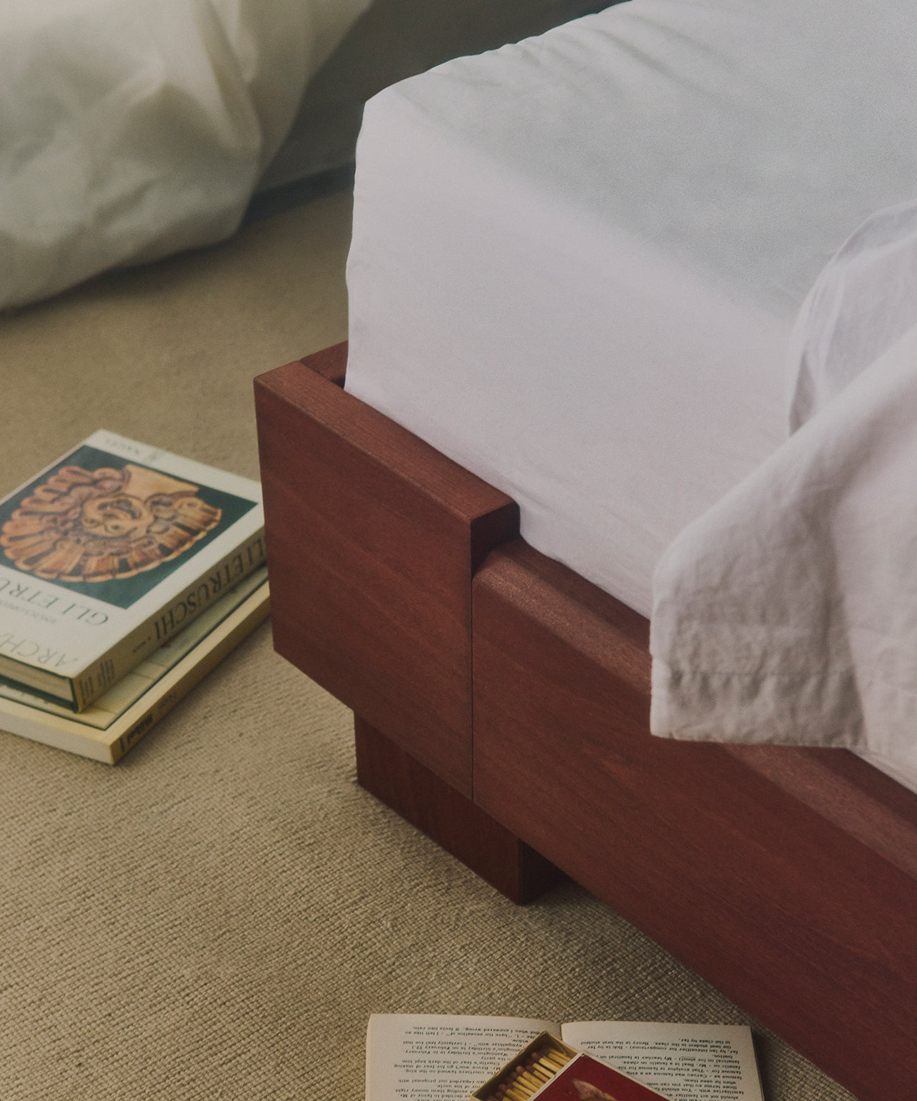 Cubico houten bedframe van Rye Sleep, met een wit matras en boeken op de grond.