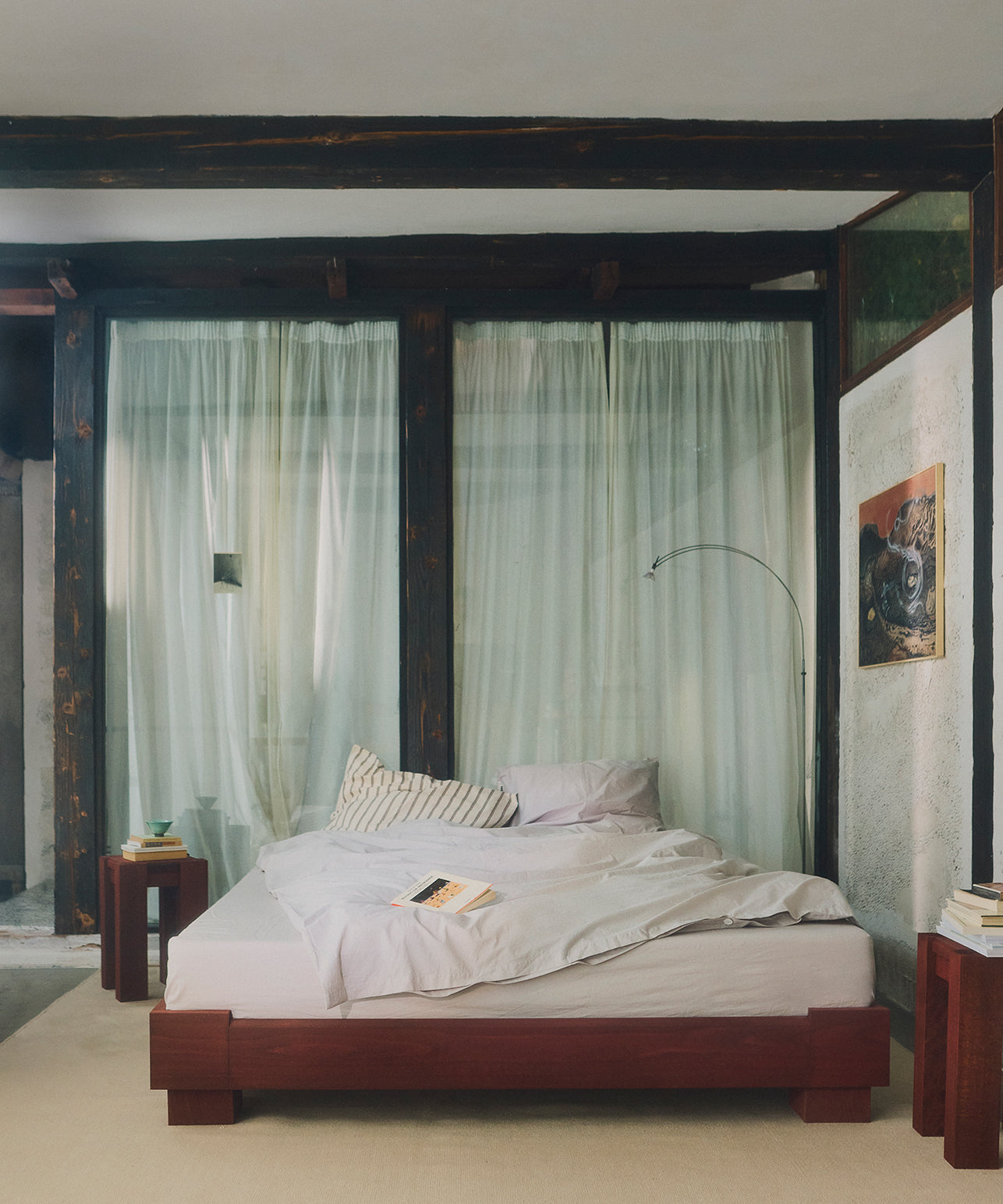 Slaapkamer met een groot houten bed, gordijnen en minimalistische decoratie.