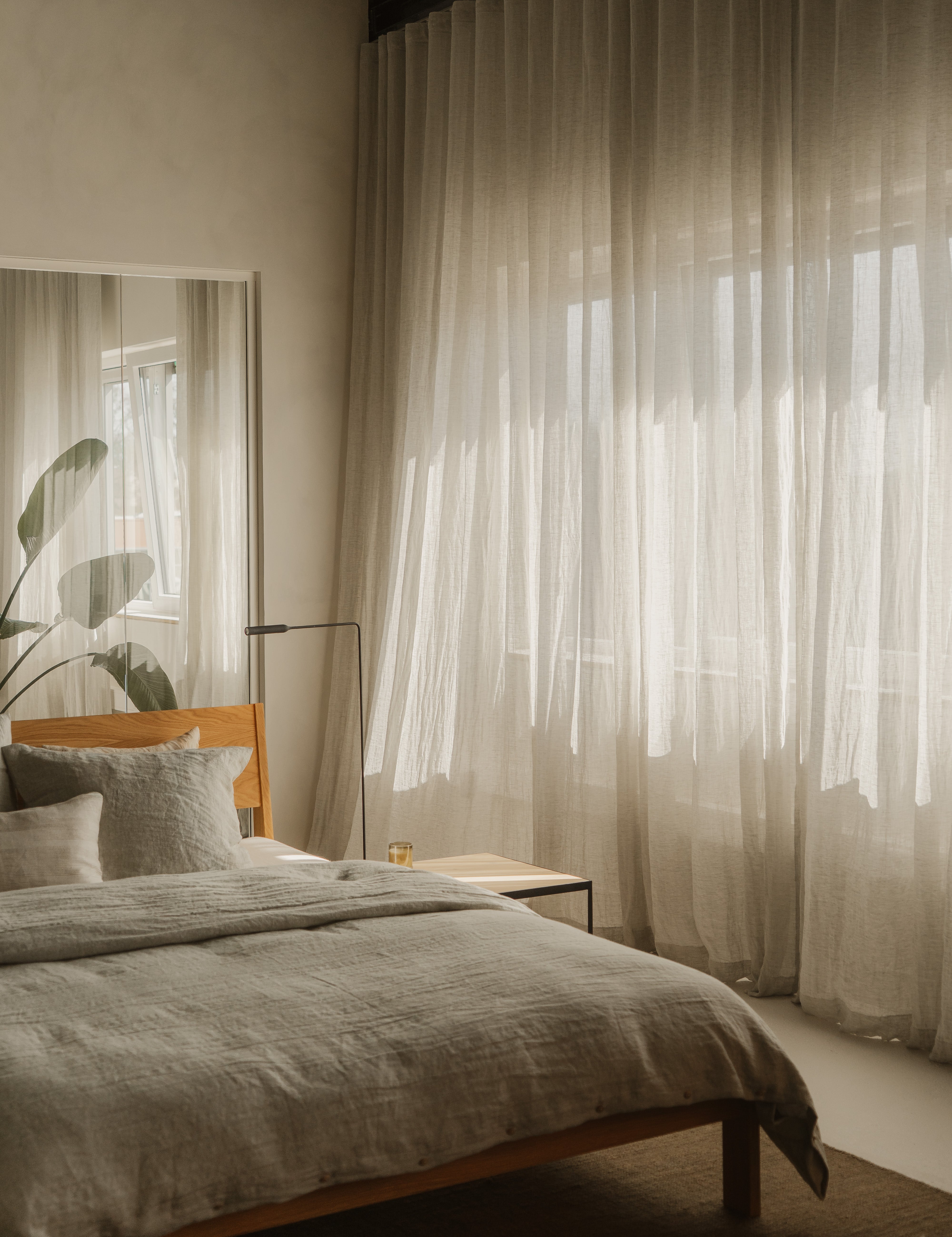 Slaapkamer met een bed, nachtkastje en een groot raam met linnen gordijnen van By Mölle.