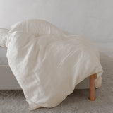 By Mölle linnen dekbedovertrek in de kleur warm white, hangend over een bed met linnen bedframe en een beige vloerkleed.
