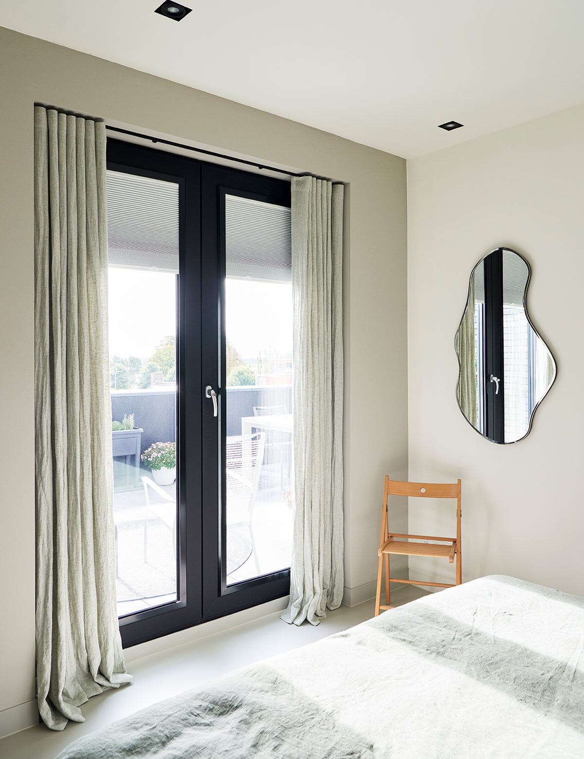 Lichtgroene By Mölle linnen gordijnen met een waveplooi, hangend in een slaapkamer met openslaande deuren naar het balkon.