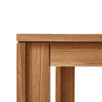 Vierkante tafel met ultra-dun tafelblad en verzonken poten van massief eikenhout. Subtiele schaduwlijn tussen blad en frame zorgt voor een licht zwevend effect. Modulair ontwerp dat meerdere tafels naadloos in een rij verbindt. Robuust en elegant, perfect voor dagelijks gebruik in moderne interieurs.