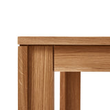 Vierkante tafel met ultra-dun tafelblad en verzonken poten van massief eikenhout. Subtiele schaduwlijn tussen blad en frame zorgt voor een licht zwevend effect. Modulair ontwerp dat meerdere tafels naadloos in een rij verbindt. Robuust en elegant, perfect voor dagelijks gebruik in moderne interieurs.