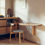 Minimalist folding wall table made of solid oak with a slender frame and concealed hinge mechanism. Oval tabletop folds away easily, ideal for small spaces.