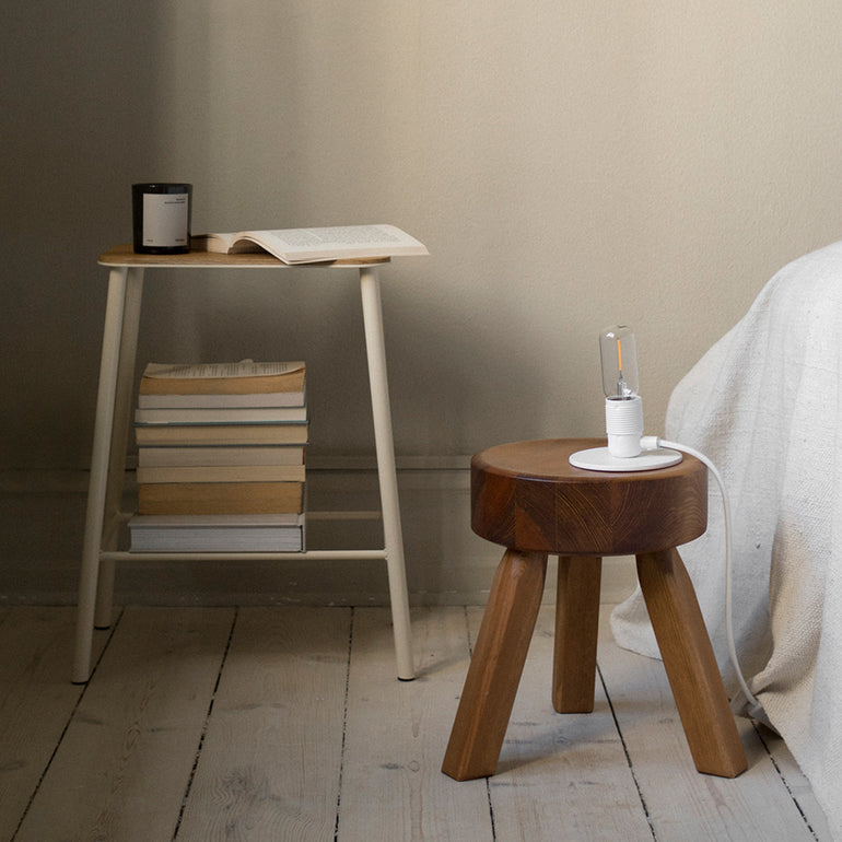 frama adam stool warm white used as a bed side table with books